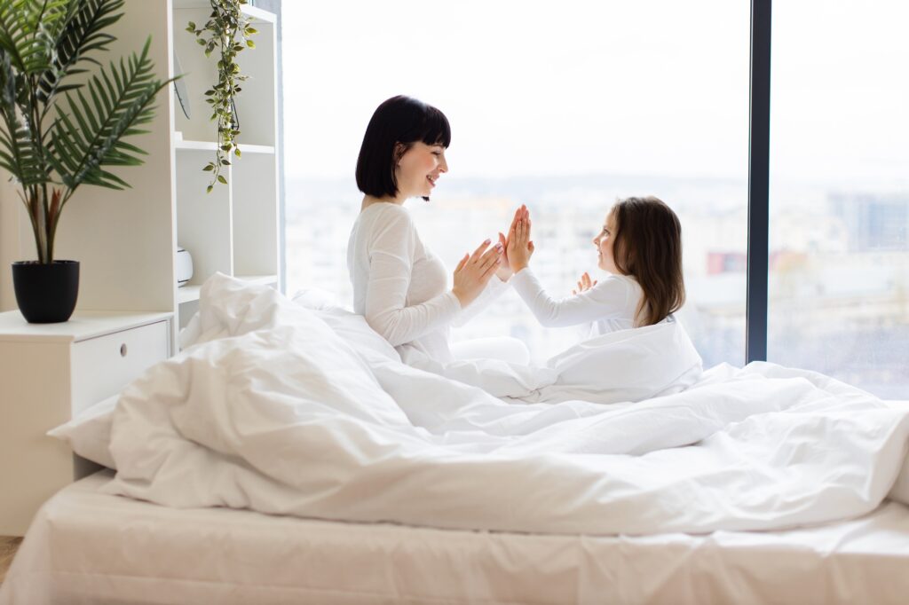 Mother and daughter playing in bed on bright morning